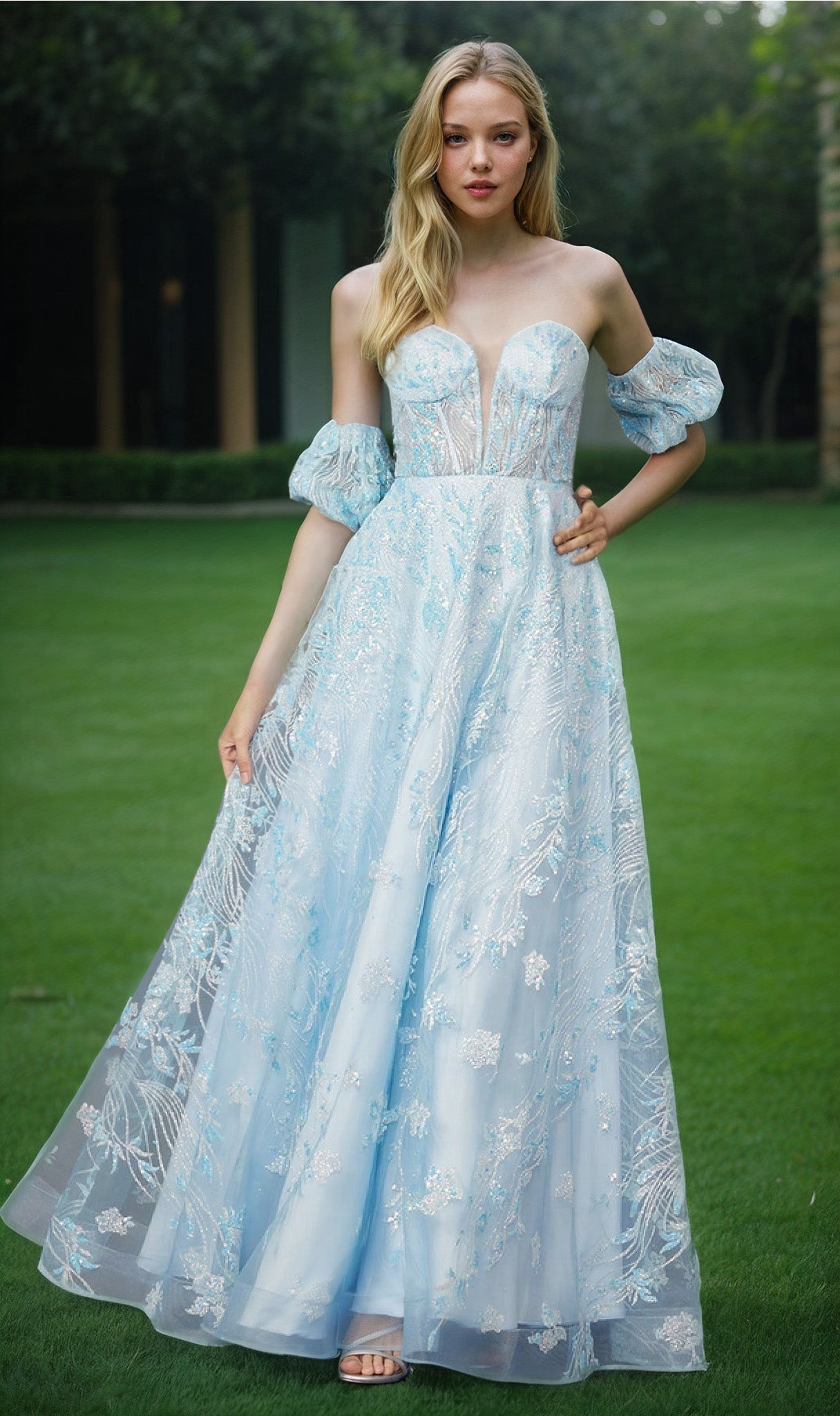 A woman stands on grass, wearing the Puff-Sleeve Strapless Long Glitter Prom Dress 2404. Trees and hedges in the background highlight the elegance of her formal attire.